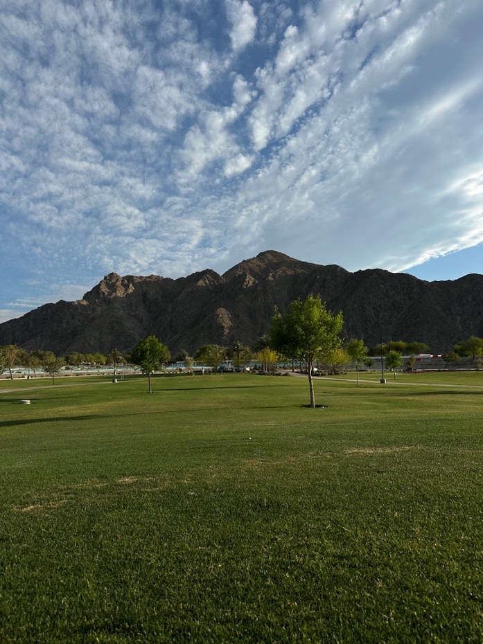 Mountains and a green field beneath a cloud-filled sky